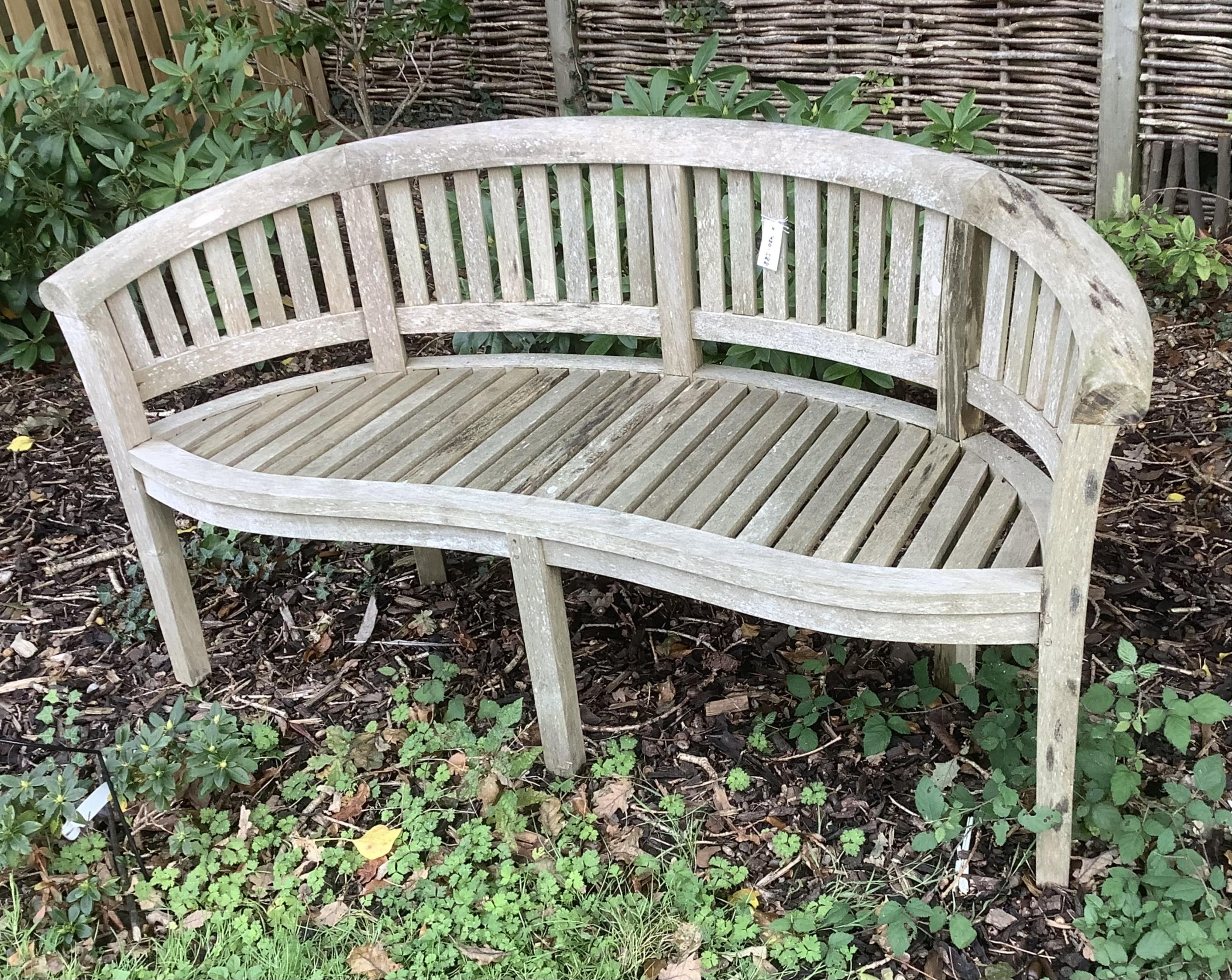 A curved teak bench, 160cm, 82cm high. Condition - weathered, otherwise good